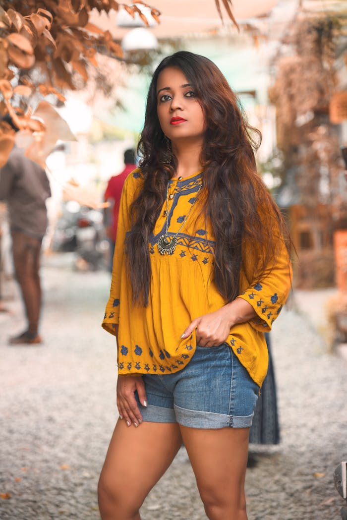 Fashionable woman posing in a vibrant yellow boho top and denim shorts outdoors.